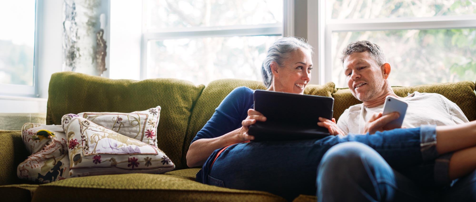 A couple sitting on the couch talking smiling holding a tablet