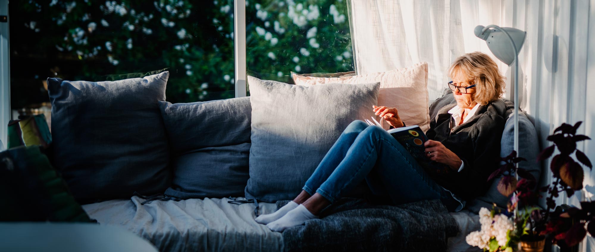 An older woman lying on the sofa reading a book