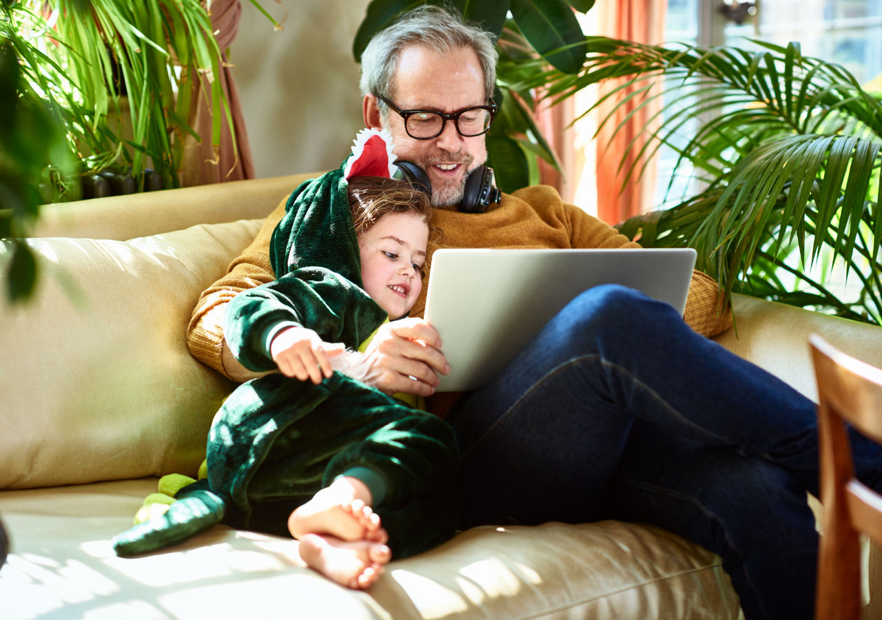 Man with a child looking at a laptop having a good time sitting on the sofa